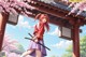 A woman with red hair stands under a traditional Japanese gate, holding a sword, surrounded by cherry blossoms.