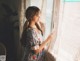 A woman standing in front of a window looking out the window.