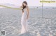 A woman in a white dress standing on a beach next to a net.