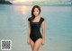 A woman in a black bathing suit standing in the water.